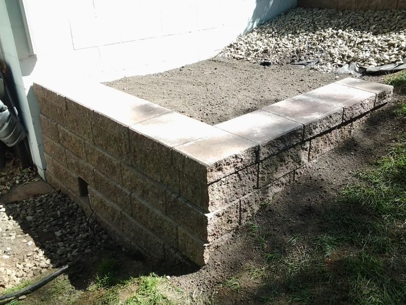 Landscaped corner retaining wall made of stone blocks, filled with soil and gravel.