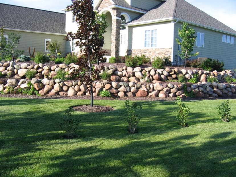 Elegant home with stone landscaping, lush green lawn, and tree accents in front yard.